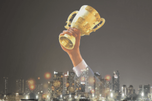 Decorative image to depict VirtueUK have been awarded one of Britain's 50 Best Managed IT Companies of 2023. Arm holding a gold trophy hovering over the image of a cityscape.