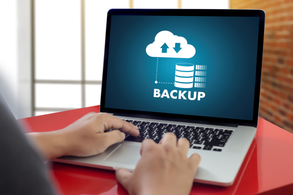 A person using a laptop displaying a "Backup" screen with a cloud and database icon, symbolizing cloud data backup.