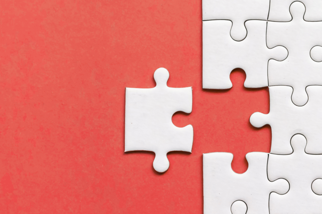 A single white puzzle piece about to be placed into a nearly completed puzzle on a red background.