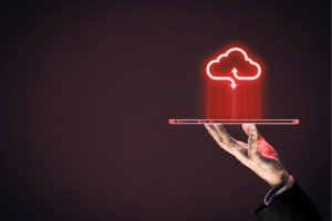 Hand holding a transparent tablet with a glowing red cloud storage icon hovering above it on a dark background.
