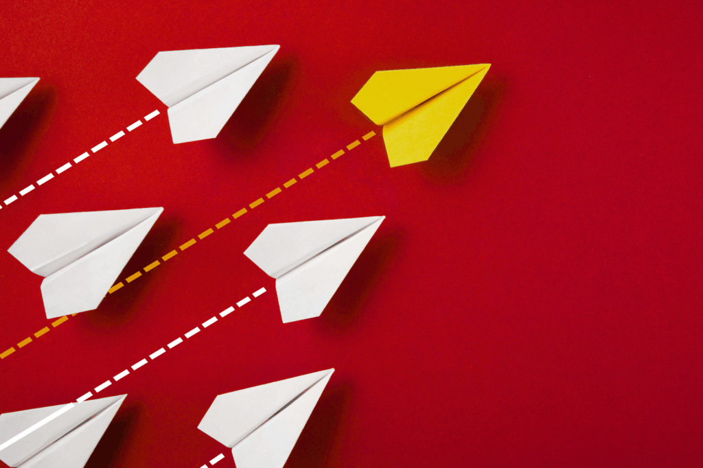 Yellow paper airplane leading white paper airplanes on a red background, symbolizing leadership and innovation.