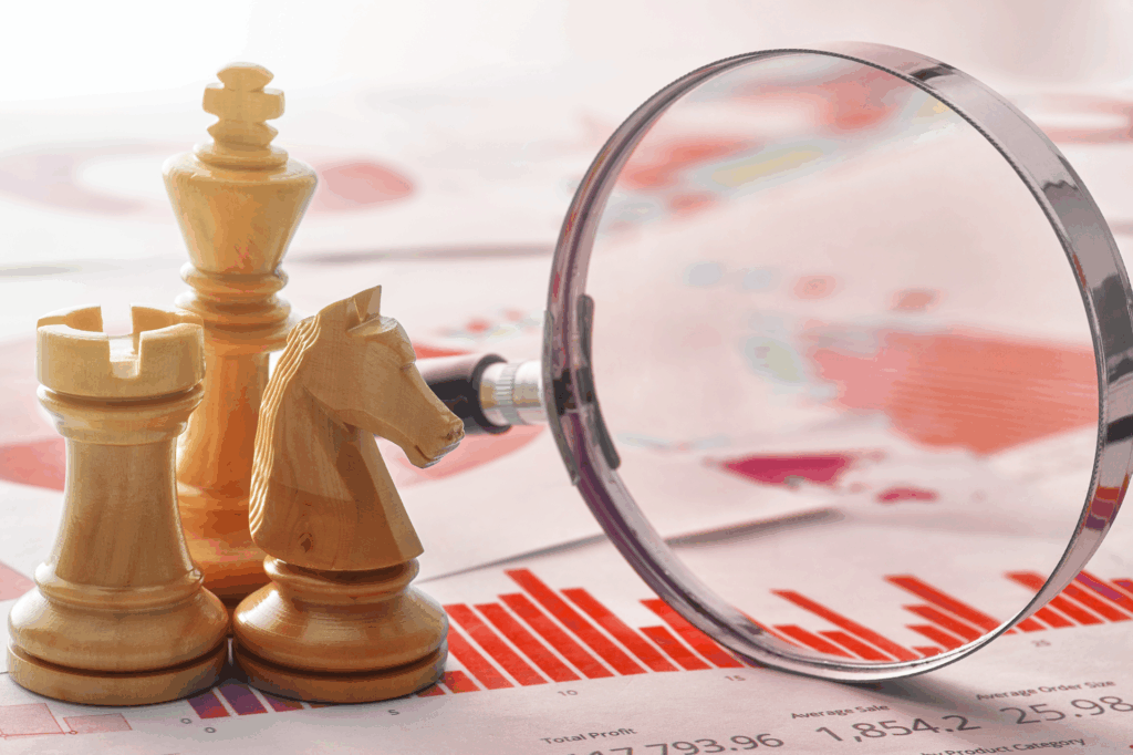 Wooden chess pieces (rook, knight, king) and a magnifying glass placed on financial graphs and bar charts, symbolising strategic planning and data analysis.
